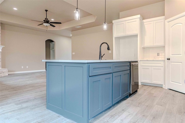 kitchen with pendant lighting, an island with sink, white cabinets, ceiling fan, and a tray ceiling