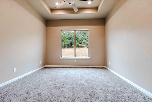 carpeted empty room with ceiling fan and a tray ceiling