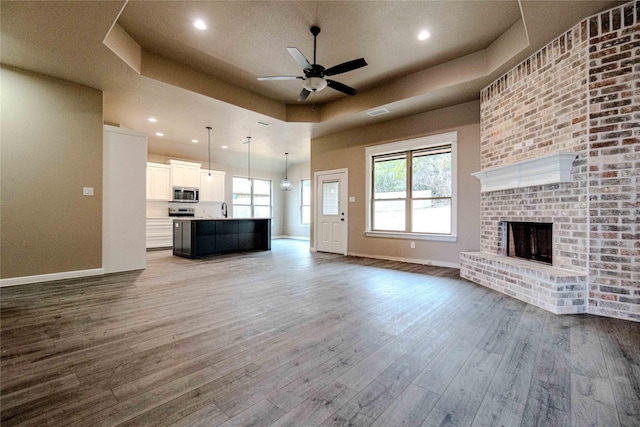 unfurnished living room with wood-type flooring, a brick fireplace, ceiling fan, and a tray ceiling