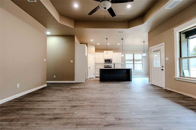 kitchen featuring white cabinetry, decorative light fixtures, light wood-type flooring, a tray ceiling, and a kitchen island with sink