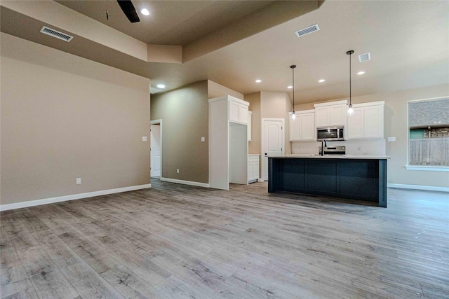 kitchen with white cabinetry, hanging light fixtures, light wood-type flooring, an island with sink, and ceiling fan