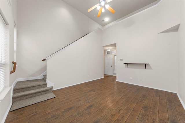 unfurnished living room with a towering ceiling, dark hardwood / wood-style floors, and ceiling fan