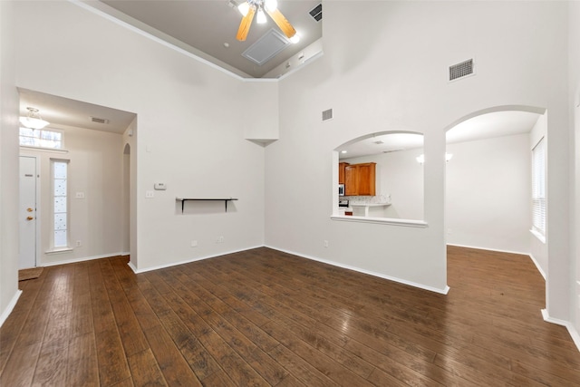 unfurnished living room featuring dark wood-type flooring, ceiling fan, and a high ceiling