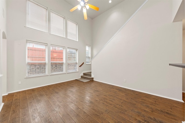 unfurnished living room featuring dark hardwood / wood-style flooring, ceiling fan, and a high ceiling