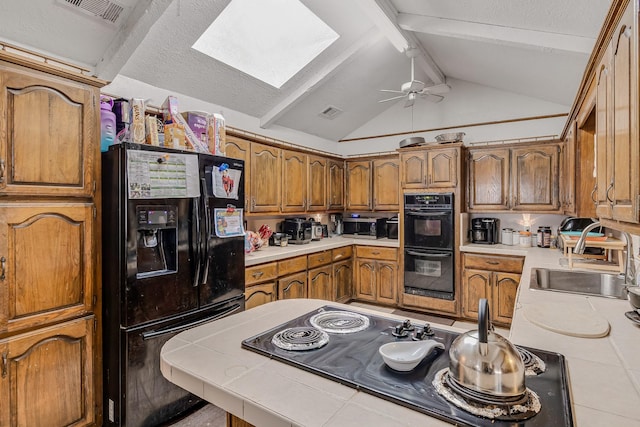 kitchen featuring lofted ceiling with skylight, tile countertops, sink, ceiling fan, and black appliances