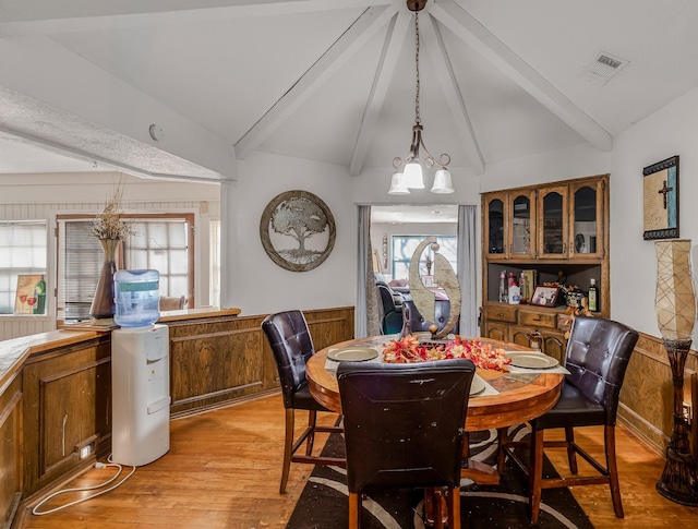 dining room featuring vaulted ceiling with beams, light hardwood / wood-style flooring, and wood walls