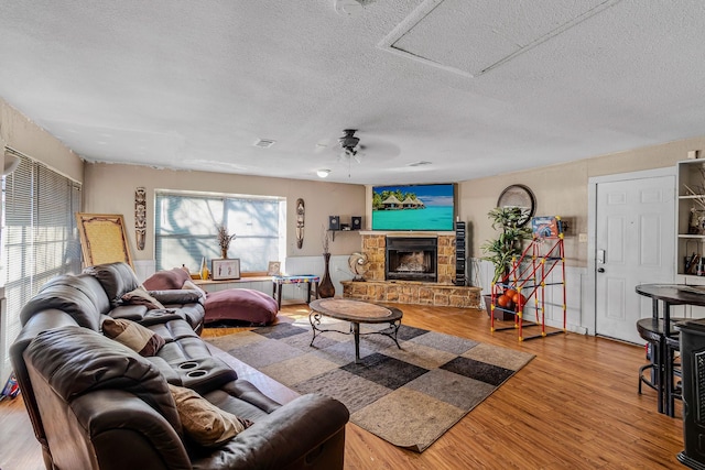 living room with hardwood / wood-style floors, a stone fireplace, a textured ceiling, and ceiling fan