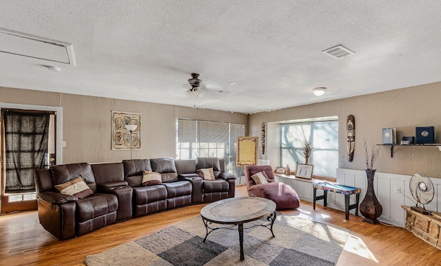 living room with a textured ceiling, ceiling fan, and light wood-type flooring