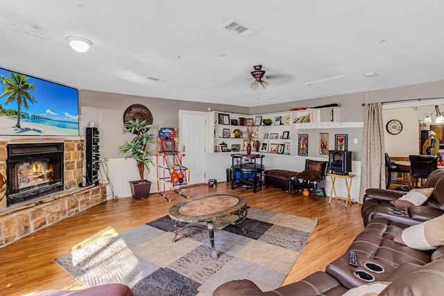 living room with ceiling fan, a stone fireplace, and light wood-type flooring