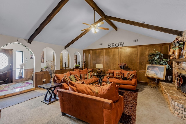 carpeted living room with wooden walls, ceiling fan, a fireplace, and lofted ceiling with beams