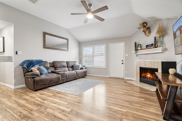 living area with lofted ceiling, light wood-style flooring, ceiling fan, a tile fireplace, and baseboards