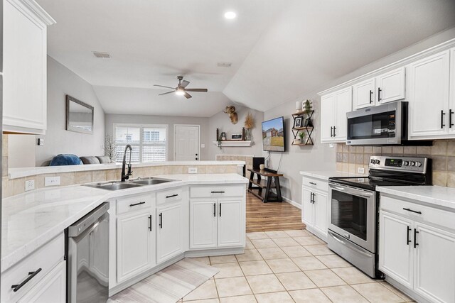 kitchen featuring a tile fireplace, white cabinetry, sink, stainless steel dishwasher, and kitchen peninsula