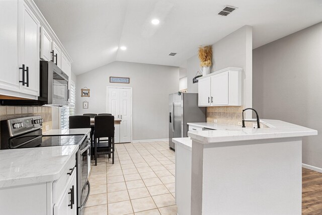 kitchen featuring a peninsula, white cabinetry, vaulted ceiling, appliances with stainless steel finishes, and tasteful backsplash