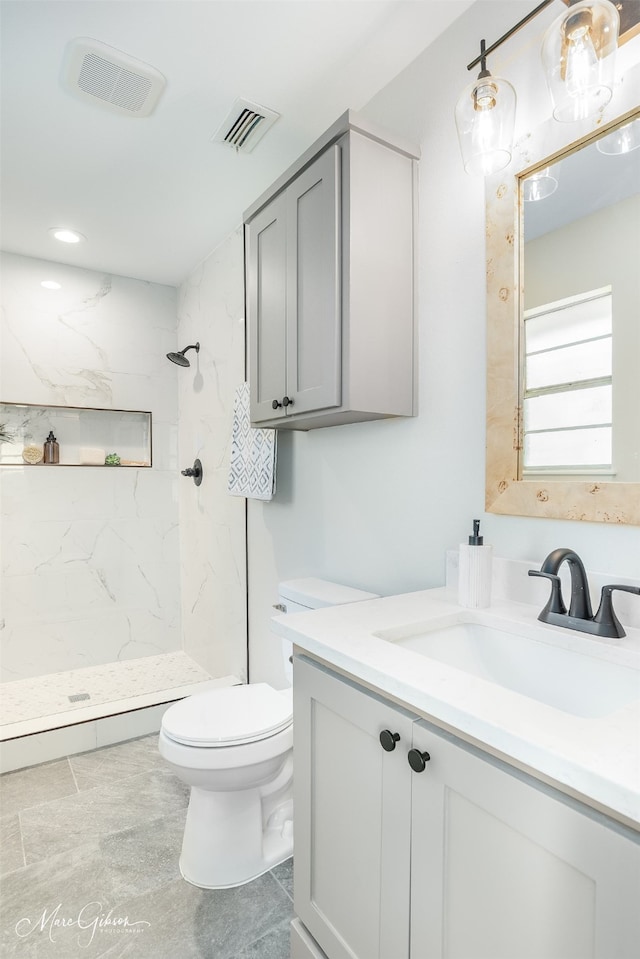 bathroom with a tile shower, vanity, and toilet