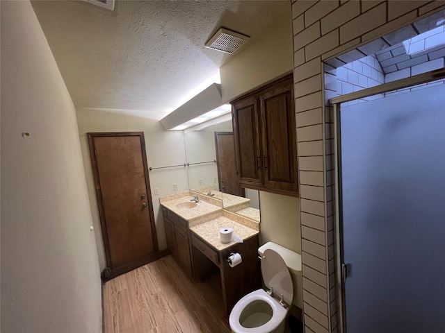 bathroom featuring hardwood / wood-style floors, vanity, a textured ceiling, a shower with shower door, and toilet