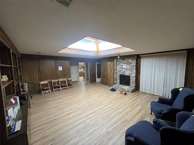 living room with a skylight, a brick fireplace, and light hardwood / wood-style flooring