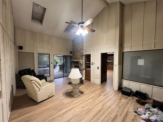 living room featuring ceiling fan, high vaulted ceiling, a fireplace, and light wood-type flooring