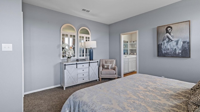 bedroom with ensuite bathroom and dark carpet