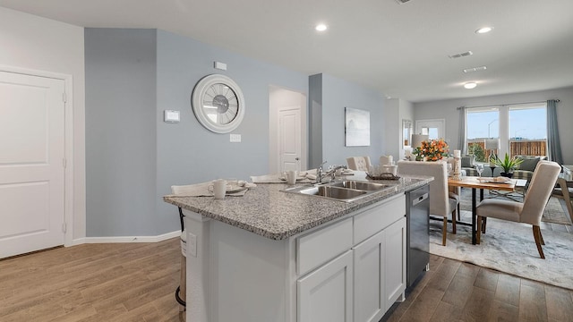 kitchen featuring dishwashing machine, sink, light hardwood / wood-style floors, an island with sink, and white cabinets