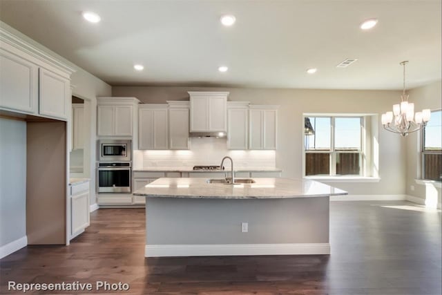 kitchen with appliances with stainless steel finishes, white cabinets, backsplash, light stone countertops, and a center island with sink