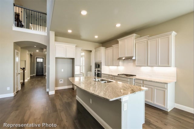 kitchen featuring white cabinetry, light stone counters, dark hardwood / wood-style floors, and an island with sink