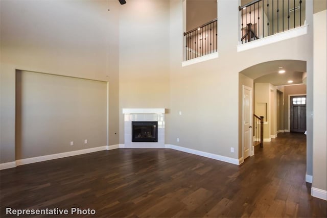 unfurnished living room with ceiling fan, dark wood-type flooring, a fireplace, and a towering ceiling