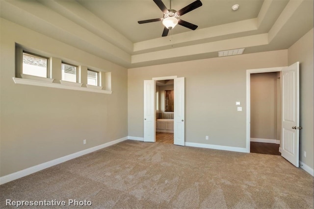 unfurnished bedroom with connected bathroom, a tray ceiling, and light colored carpet