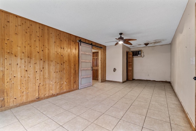 tiled empty room featuring a barn door, a textured ceiling, ceiling fan, and wood walls