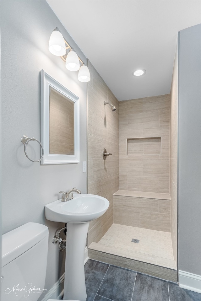 bathroom with tile patterned flooring, a tile shower, and toilet