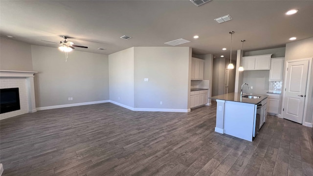 kitchen with a fireplace, an island with sink, sink, white cabinets, and dark wood-type flooring