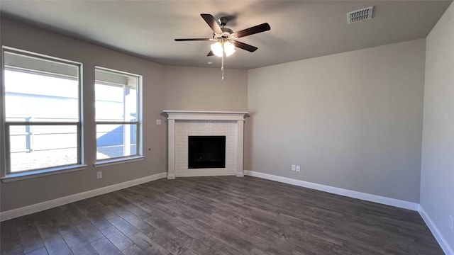 unfurnished living room featuring a healthy amount of sunlight, a brick fireplace, dark hardwood / wood-style floors, and ceiling fan