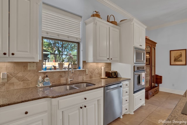 kitchen with appliances with stainless steel finishes, white cabinetry, sink, dark stone counters, and ornamental molding