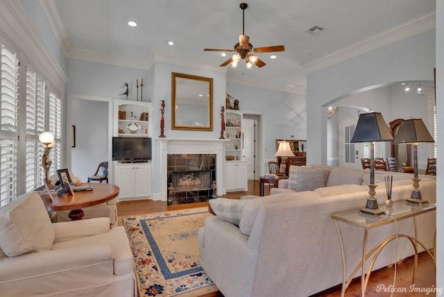 living room with ceiling fan, ornamental molding, a fireplace, and light wood-type flooring