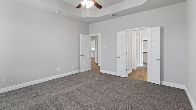 unfurnished bedroom with a raised ceiling, carpet, and ceiling fan