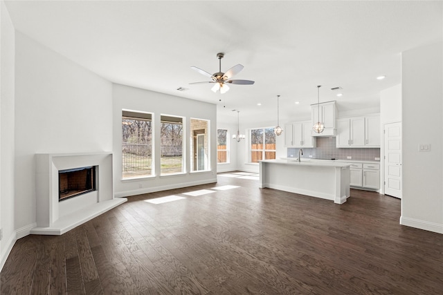 unfurnished living room with sink, dark hardwood / wood-style flooring, and ceiling fan with notable chandelier