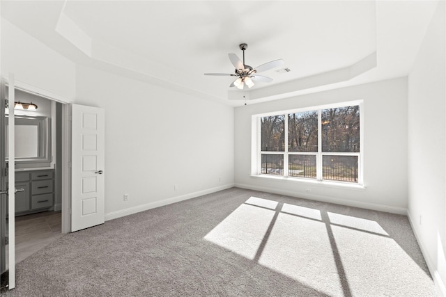 unfurnished bedroom with carpet, connected bathroom, ceiling fan, and a tray ceiling