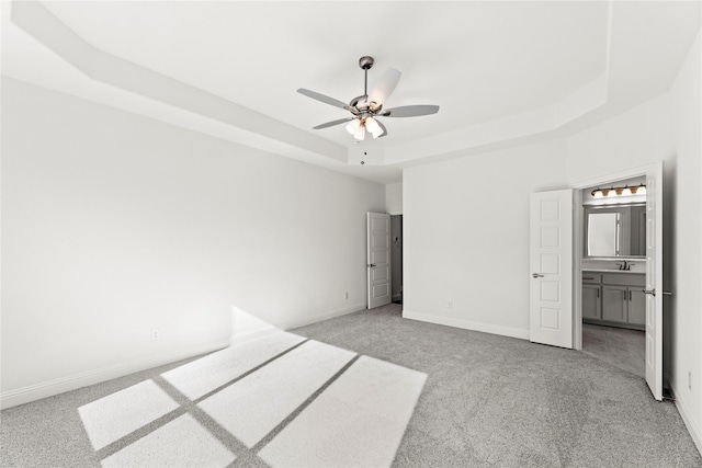 unfurnished bedroom with light carpet, sink, ensuite bath, and a raised ceiling