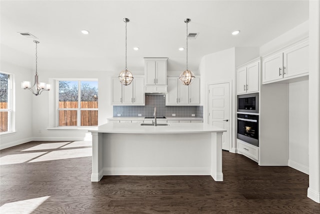 kitchen featuring stainless steel oven, a kitchen island with sink, black microwave, and white cabinets