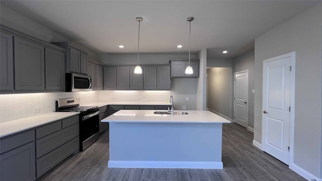 kitchen featuring gray cabinets, decorative light fixtures, sink, stainless steel appliances, and a center island with sink