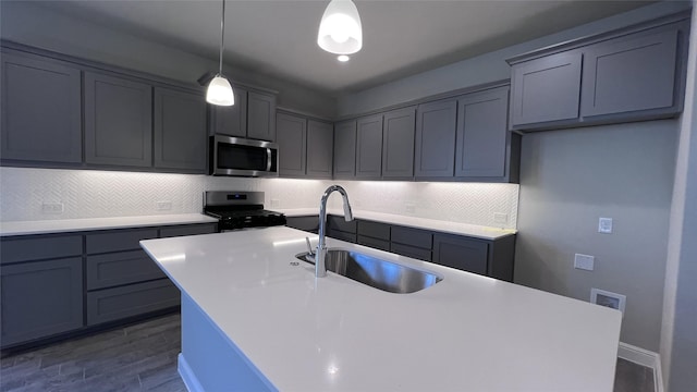 kitchen featuring sink, decorative light fixtures, stainless steel appliances, a kitchen island with sink, and backsplash