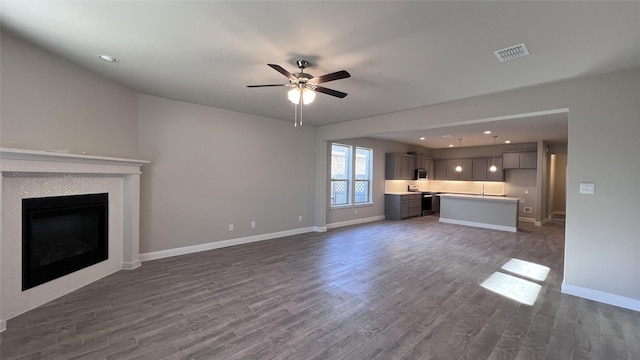 unfurnished living room featuring ceiling fan, a fireplace, and dark hardwood / wood-style flooring