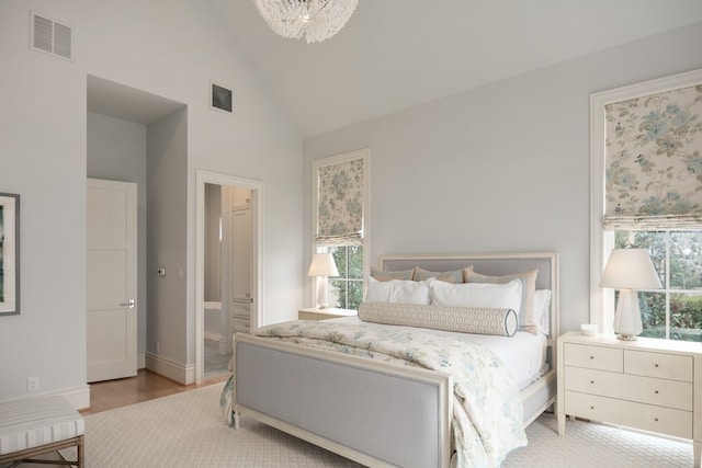 bedroom with an inviting chandelier, ensuite bathroom, high vaulted ceiling, and multiple windows