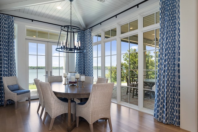 dining area featuring hardwood / wood-style floors, beamed ceiling, a chandelier, a water view, and french doors