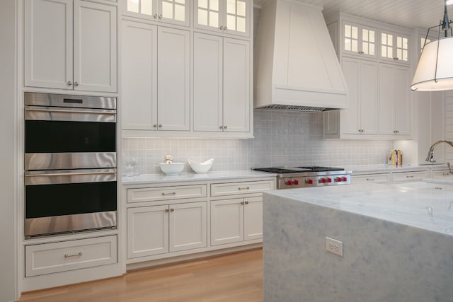 kitchen featuring pendant lighting, appliances with stainless steel finishes, white cabinets, and premium range hood