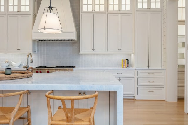 kitchen featuring white cabinetry, hanging light fixtures, custom exhaust hood, and a kitchen breakfast bar