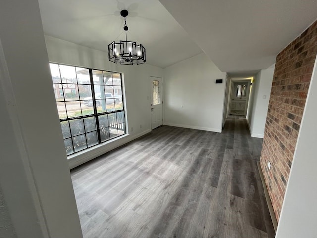 unfurnished dining area with an inviting chandelier, hardwood / wood-style flooring, and brick wall