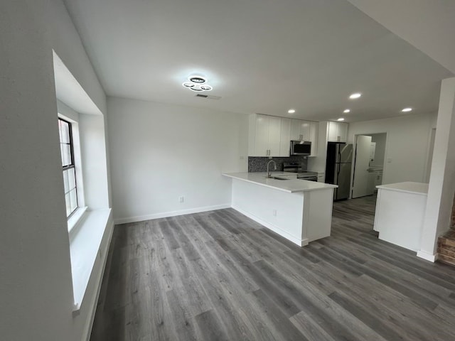 kitchen with stainless steel appliances, kitchen peninsula, wood-type flooring, and white cabinets