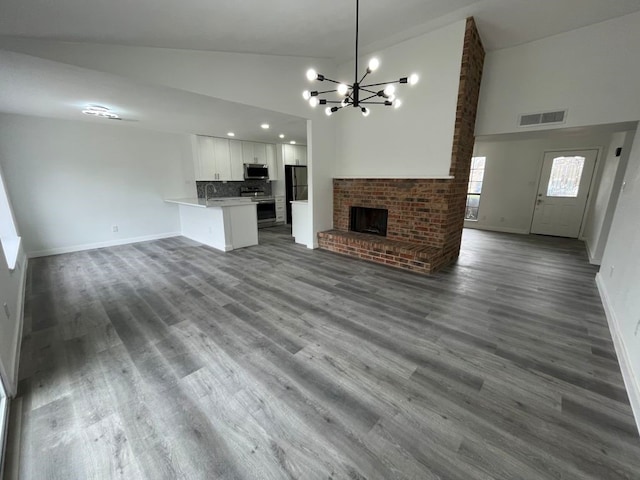 unfurnished living room featuring hardwood / wood-style flooring, a chandelier, high vaulted ceiling, and a brick fireplace