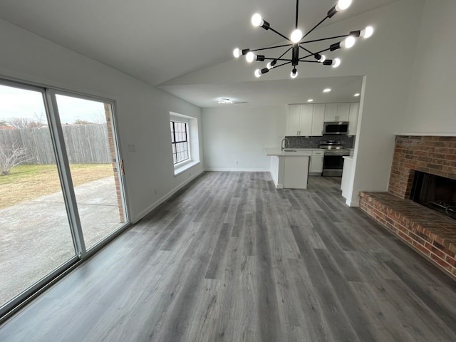 unfurnished living room featuring a brick fireplace, a notable chandelier, vaulted ceiling, and wood-type flooring