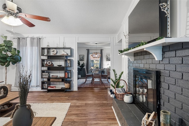 living room with ceiling fan, dark hardwood / wood-style floors, a fireplace, ornamental molding, and a textured ceiling